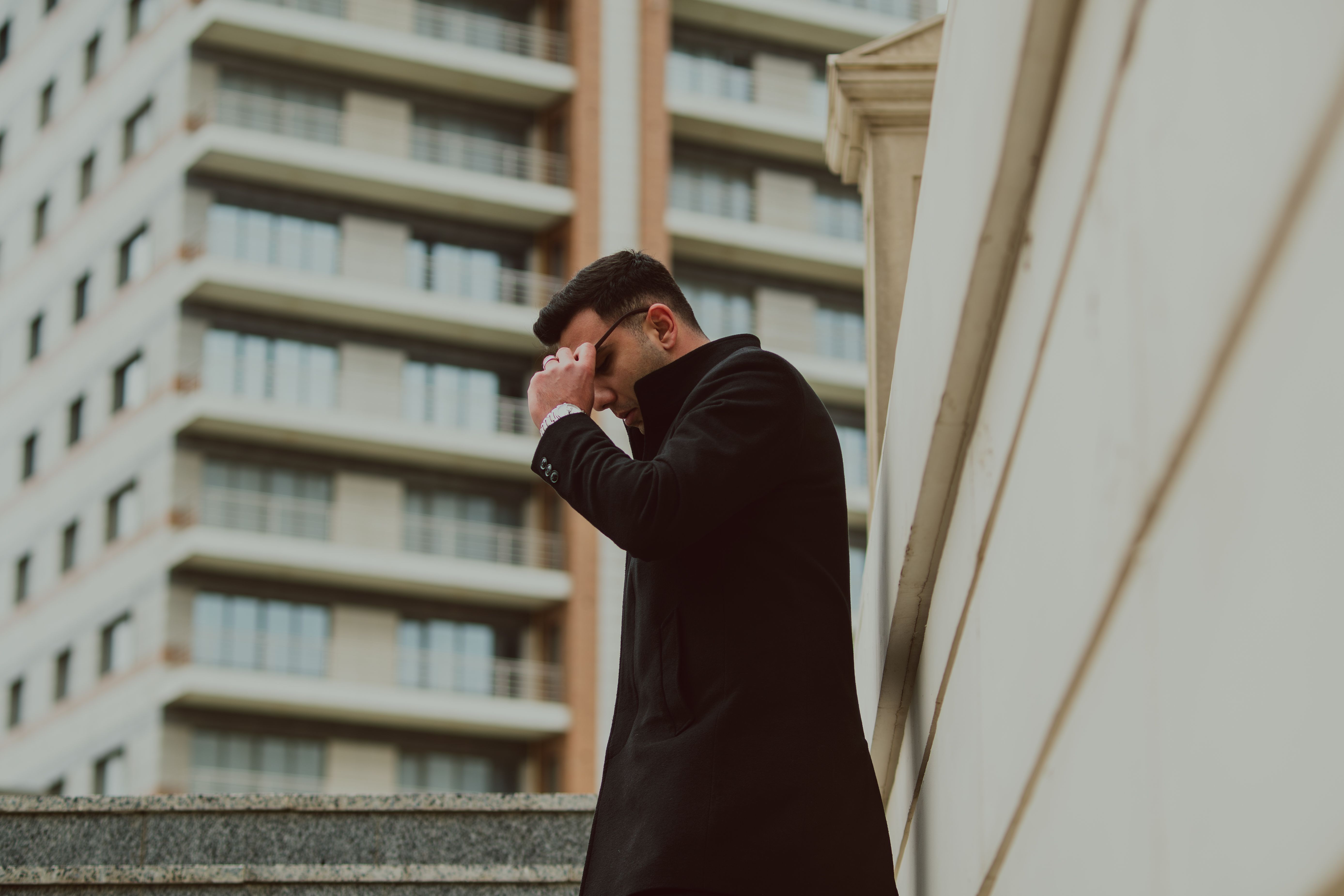 Elegant man in black coat standing in urban environment with modern buildings.
