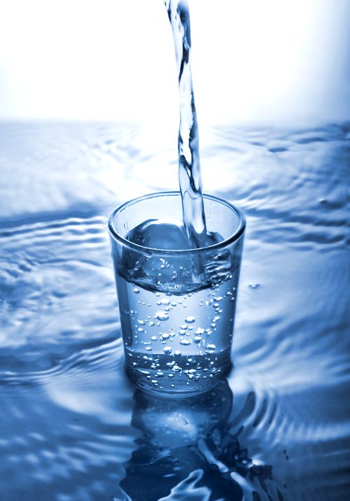 Free A vertical shot of water pouring into a glass, creating ripples in a serene blue setting. Stock Photo