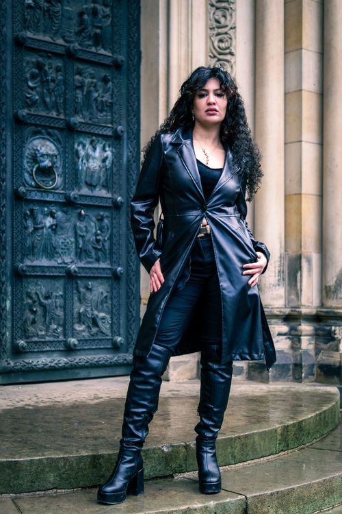 Free Stylish woman in black leather coat and boots poses in front of a historical door. Stock Photo