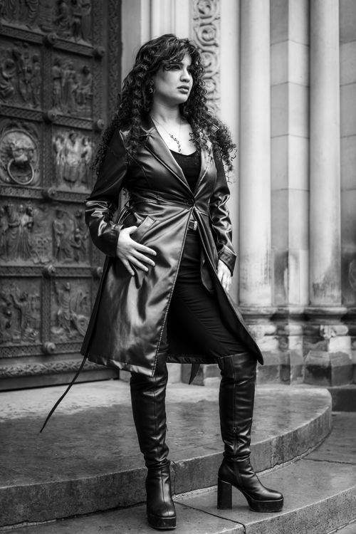 Free A fashionable woman stands confidently in a black leather coat and boots against a historic building. Stock Photo