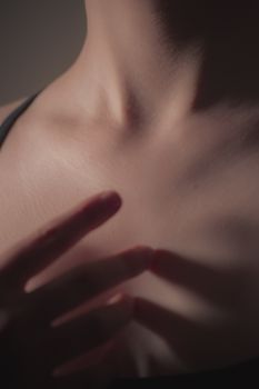 Artistic close-up photo of a woman's neck and hand with soft shadows and smooth skin.