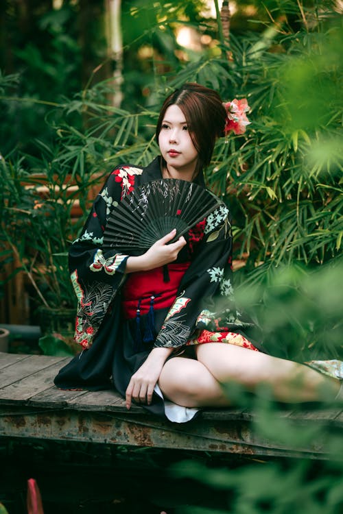 A woman in a kimono sitting on a bench with a fan