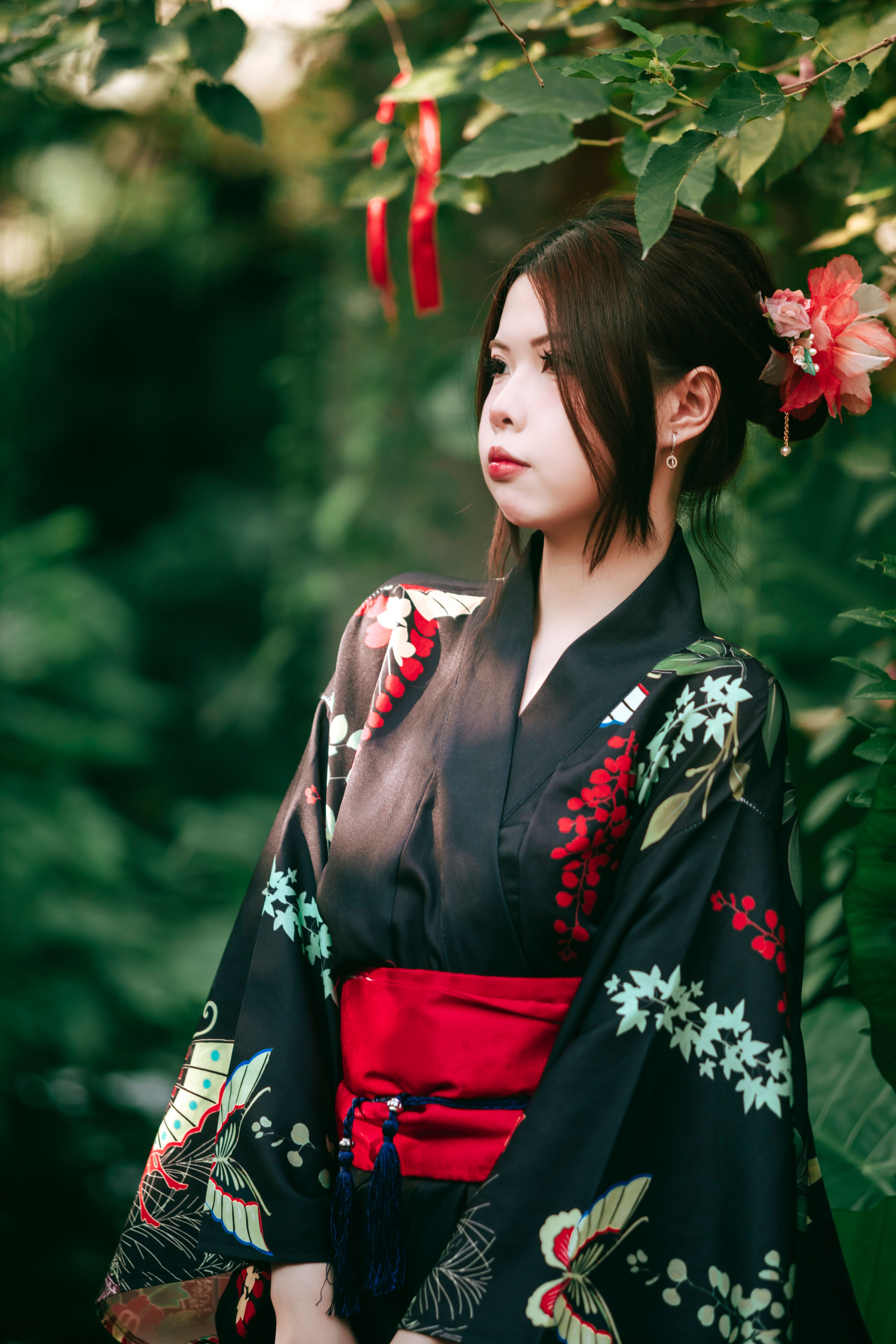 Young woman in a traditional floral kimono posing elegantly in a lush garden setting.