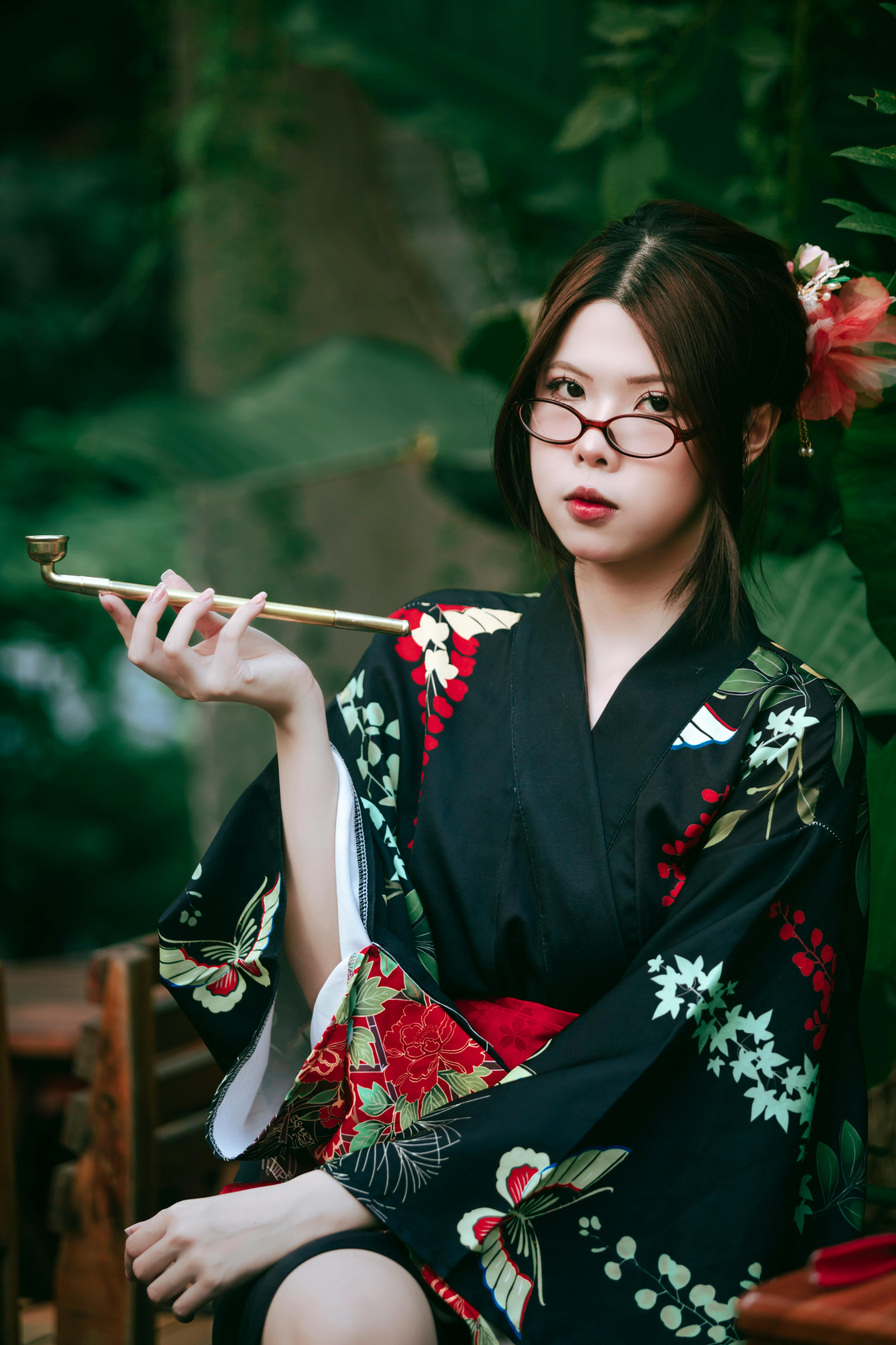 Portrait of a woman in a black floral kimono with a traditional pipe, exuding elegance against a lus