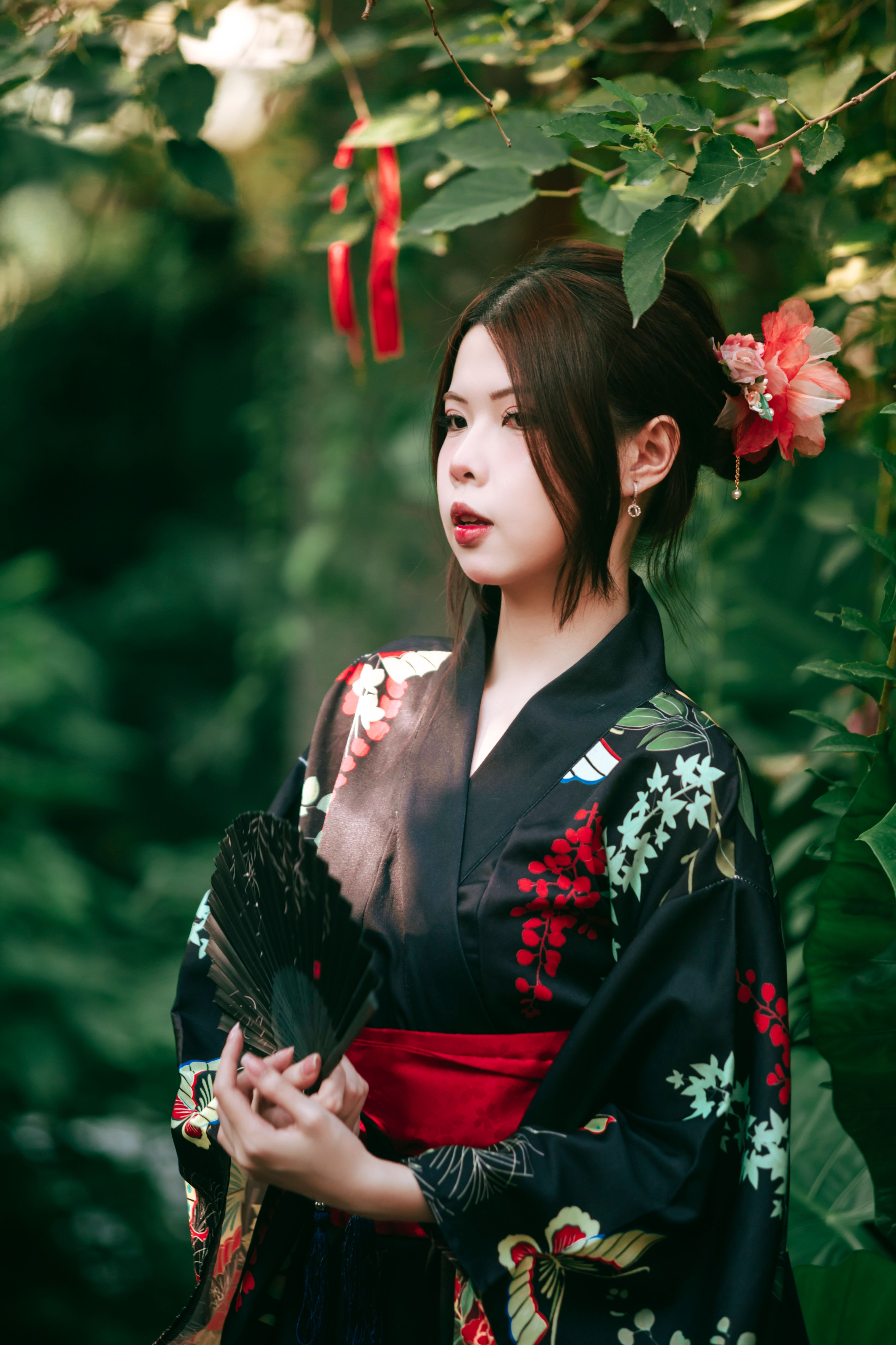 Elegant young woman in a traditional floral kimono posing gracefully in a lush garden.