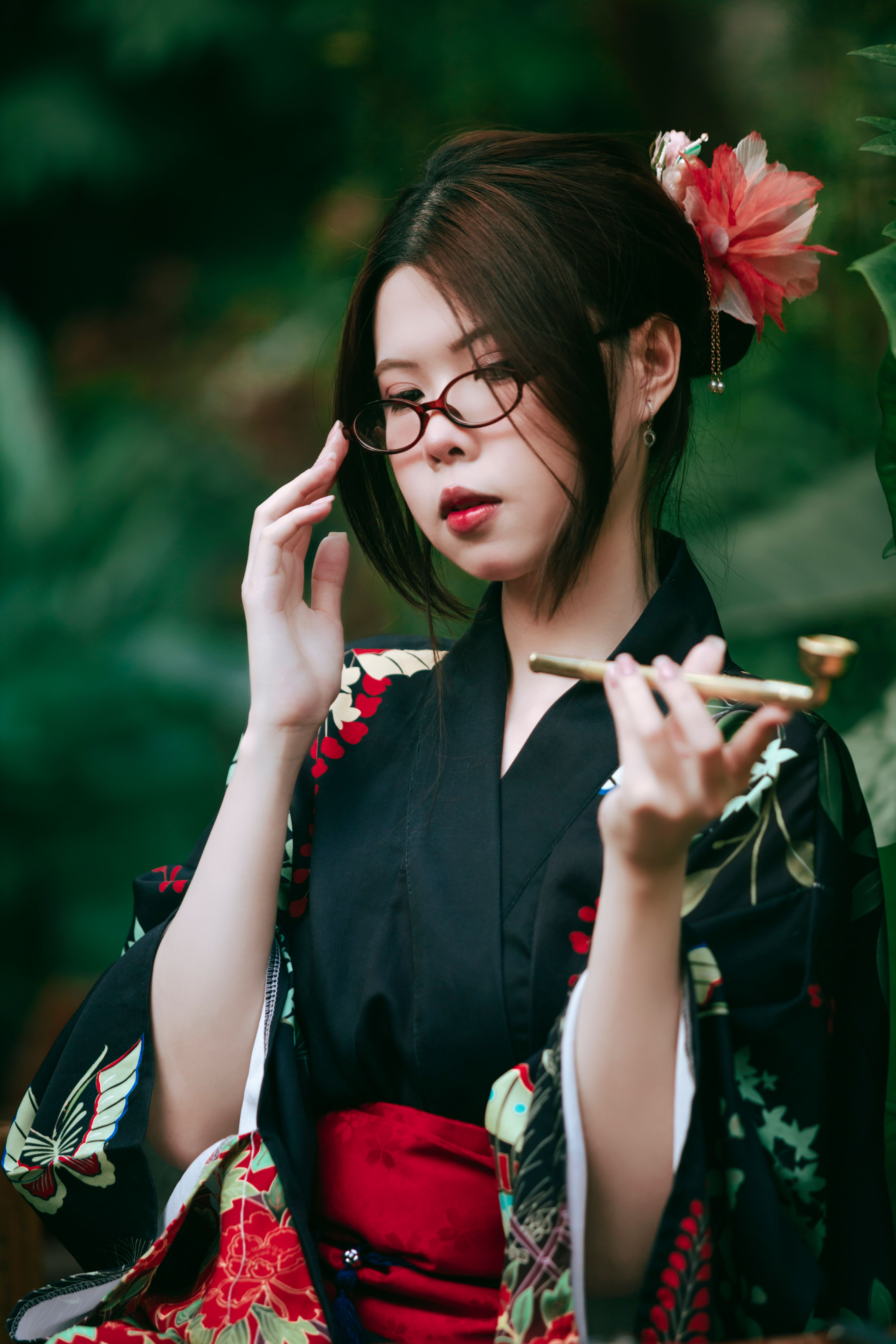 Asian woman in a kimono with glasses holding a pipe in a tranquil outdoor setting.