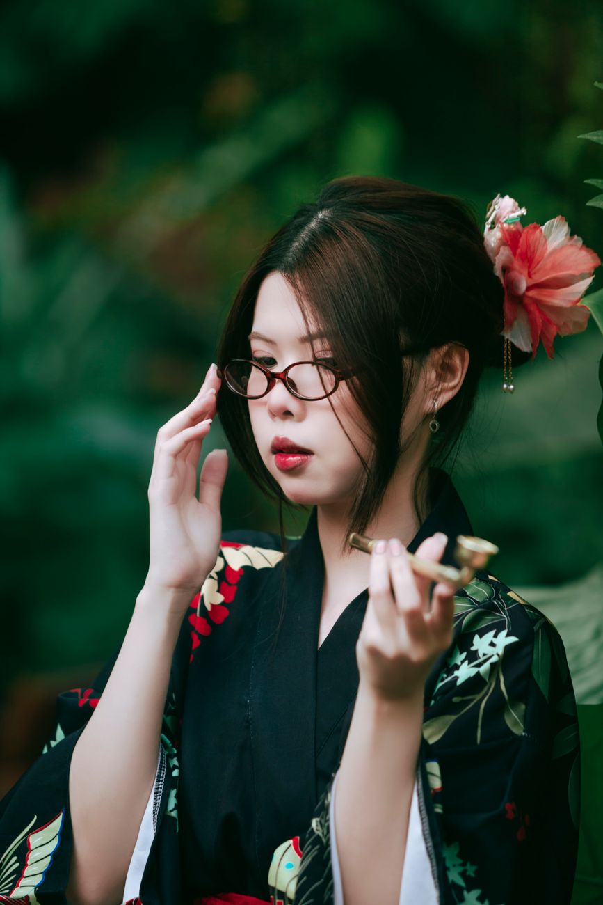Elegant portrait of a woman in a traditional kimono, holding a pipe with lush greenery background.
