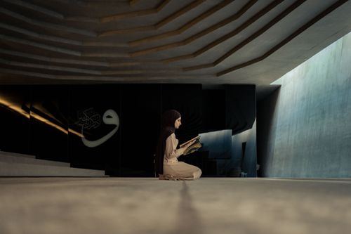 Free A woman in a hijab kneels while reading the Quran in a contemporary mosque setting. Stock Photo