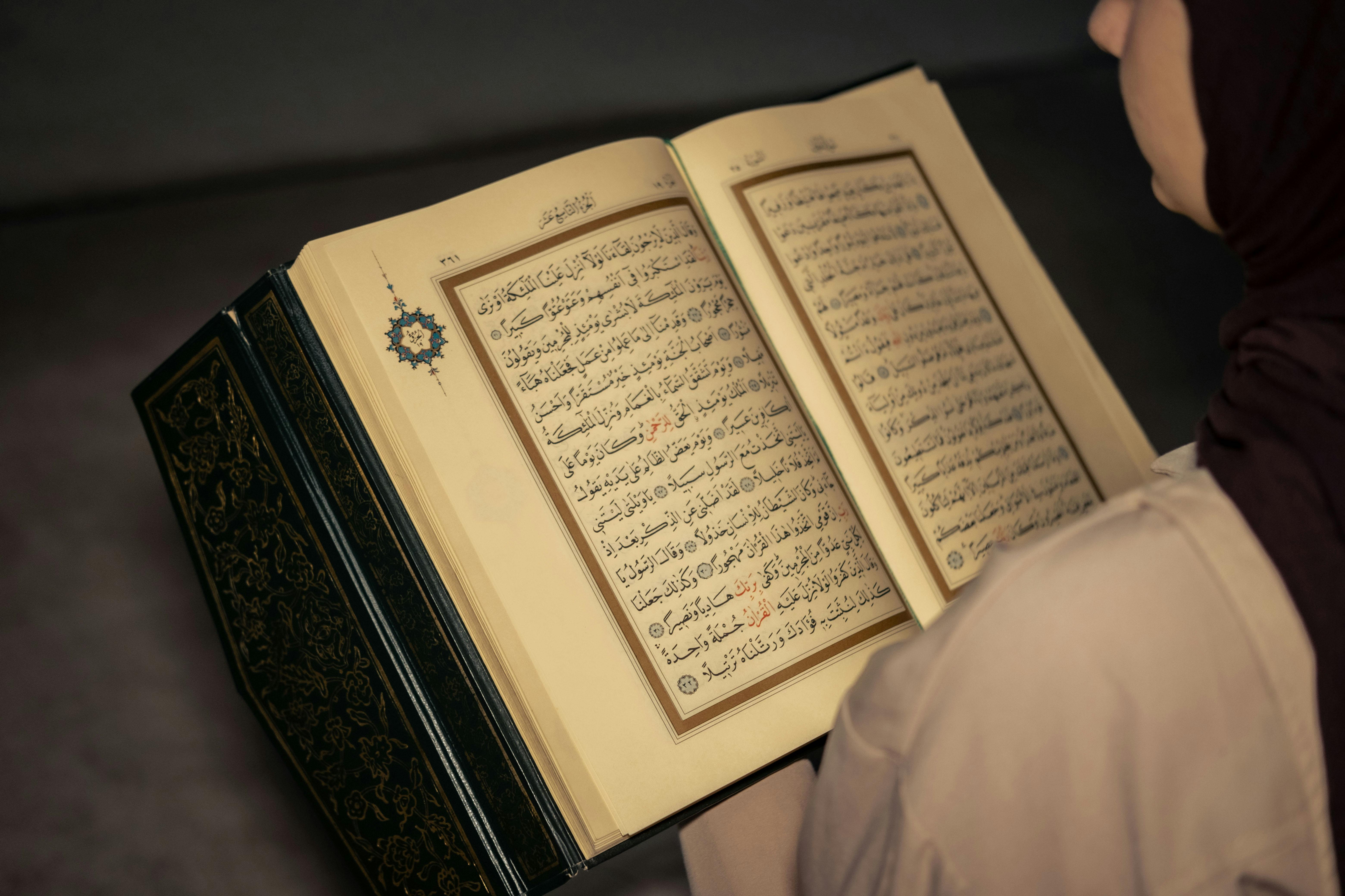 A woman wearing a hijab reads the Quran indoors, highlighting peaceful reflection.