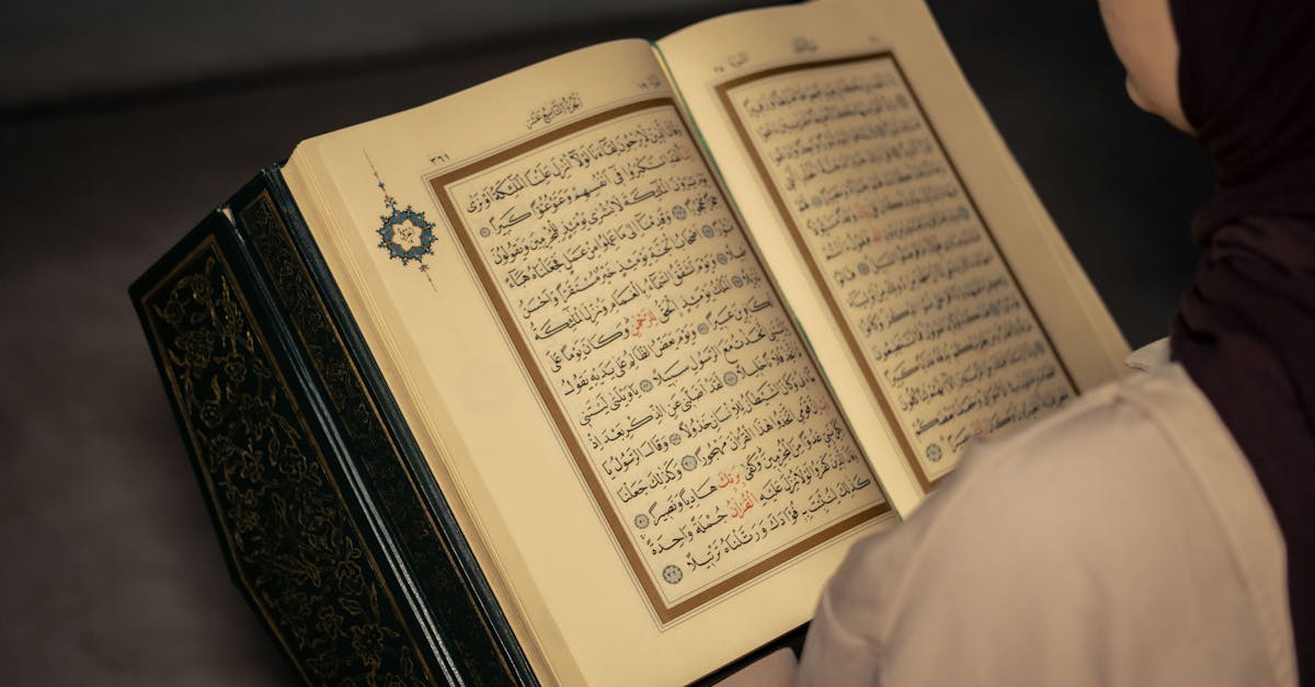 A woman wearing a hijab reads the Quran indoors, highlighting peaceful reflection.