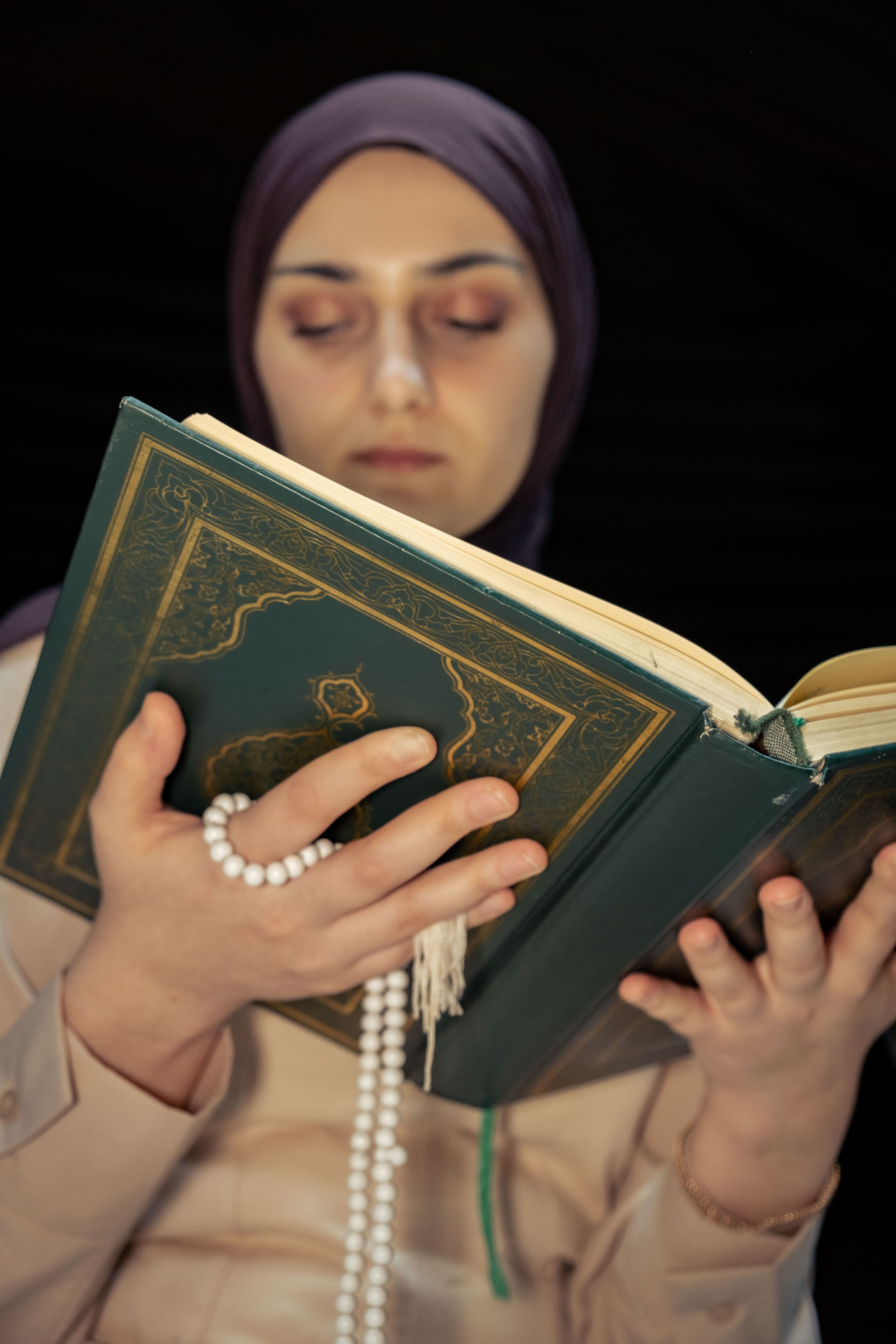 Muslim woman reading the Quran holding prayer beads