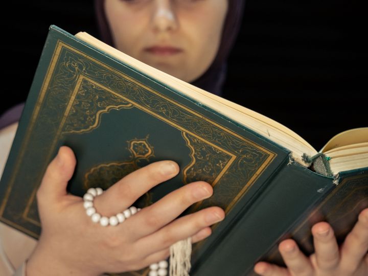 Muslim woman reading the Quran holding prayer beads