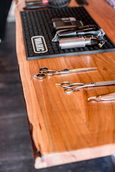 Close-up of barber tools including scissors and electric shavers laid out on a wooden table.