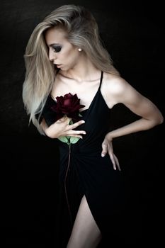 Portrait of a blonde woman in a black dress holding a red rose, showcasing elegance and fashion.