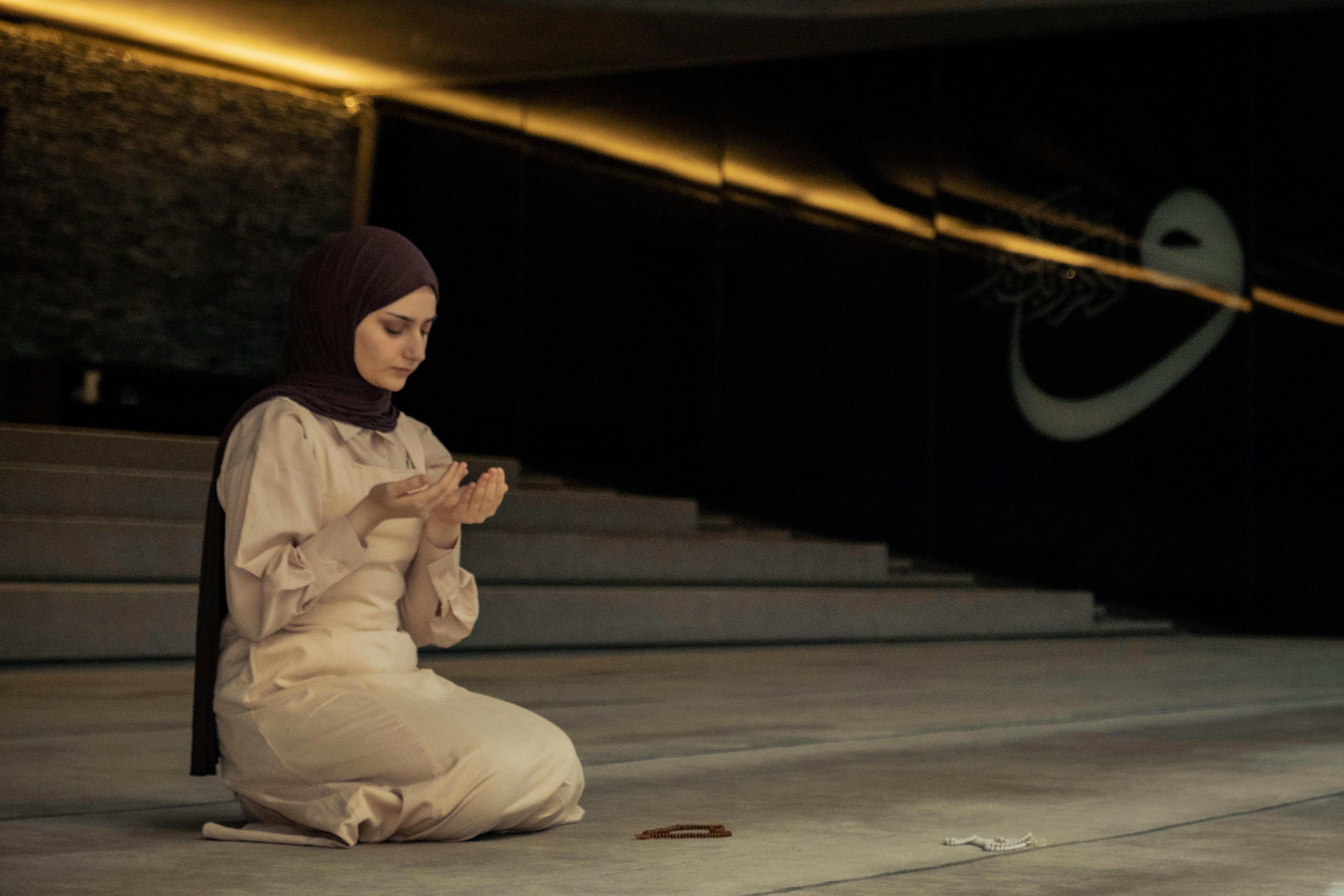 A Muslim woman kneels in prayer at a contemporary mosque, embodying tranquility and devotion.