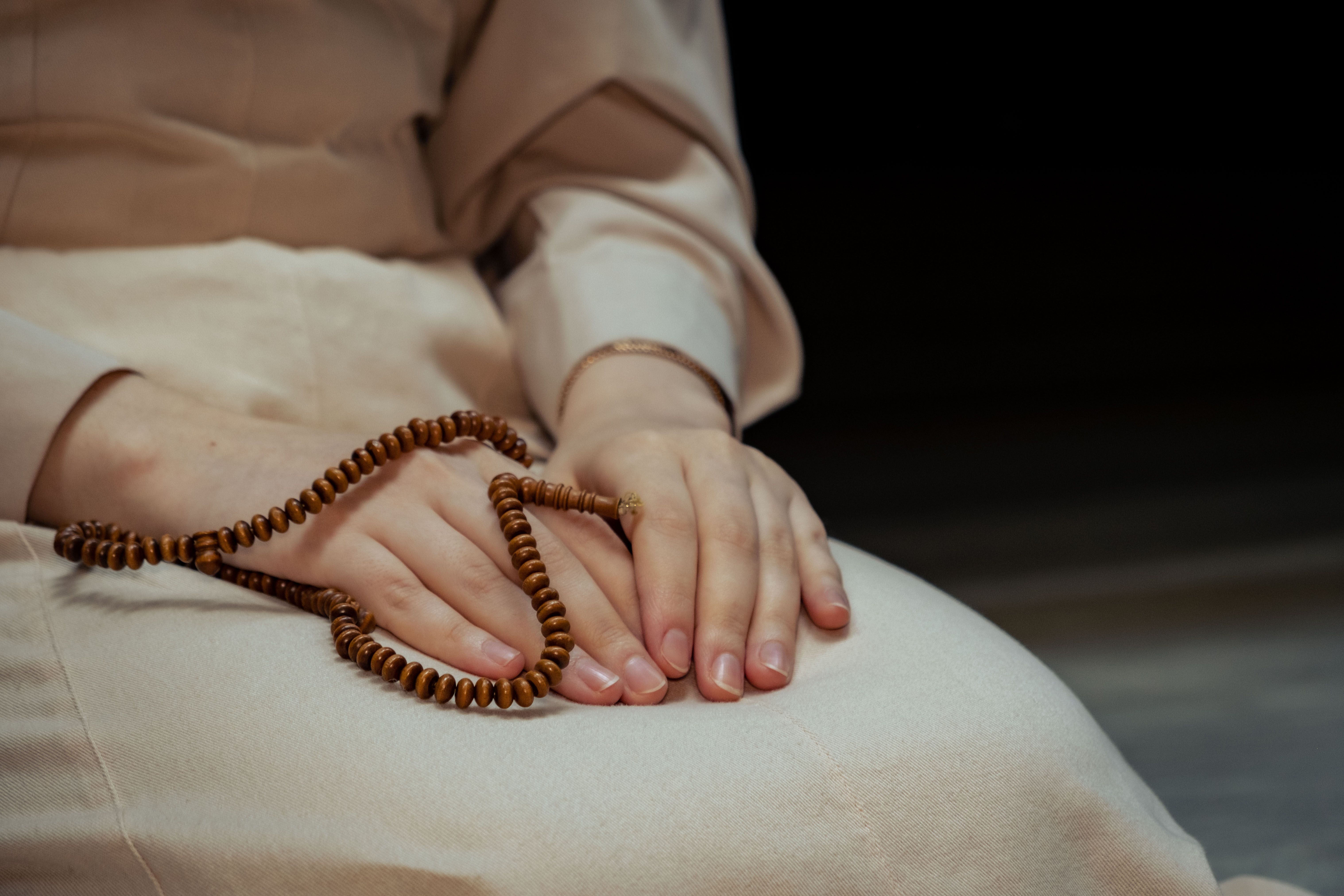 Close-up of hands in a lap, one holding prayer beads, with soft focus in the background