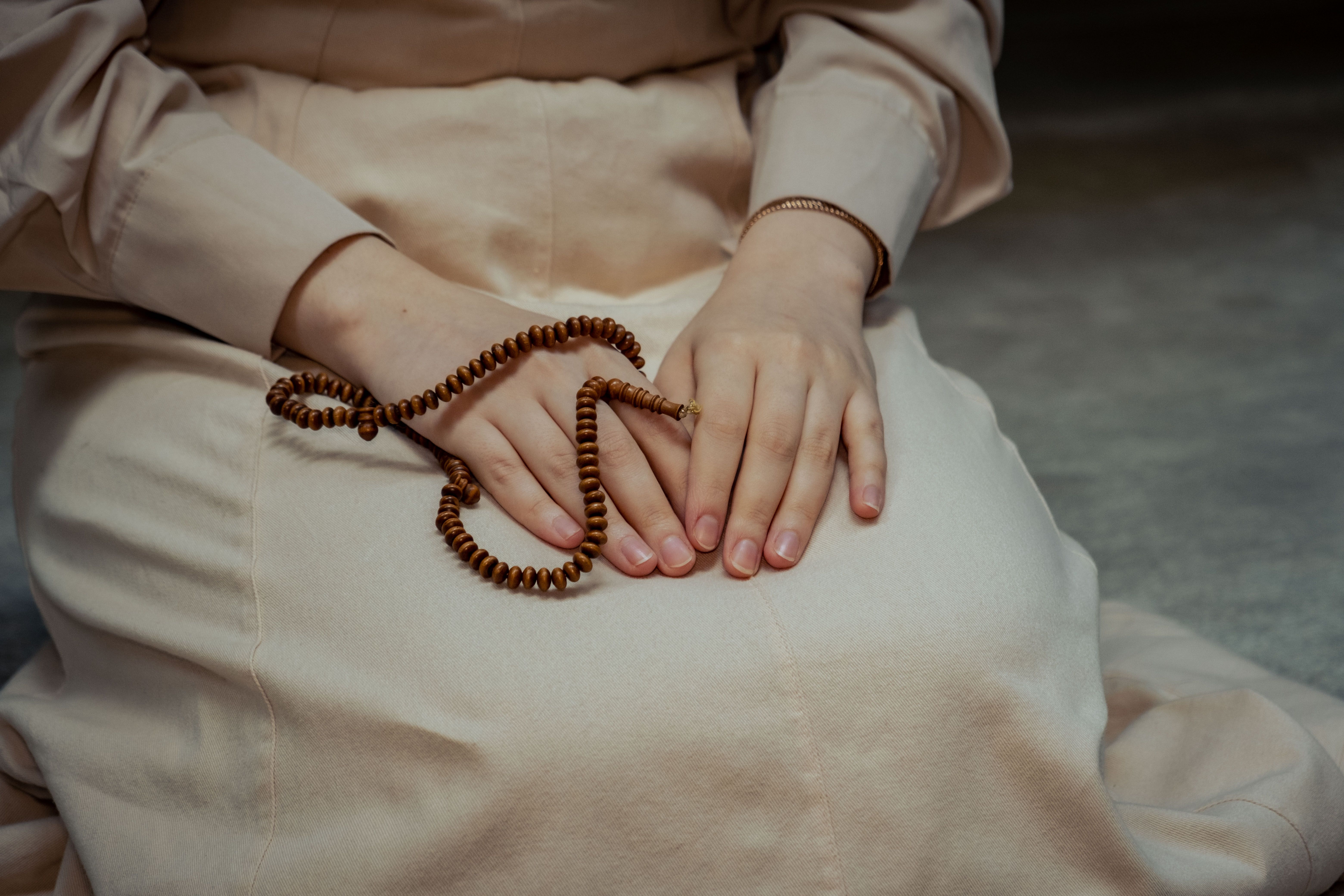 Gros plan sur les mains d'une femme tenant des perles de prière, symbolisant la dévotion.