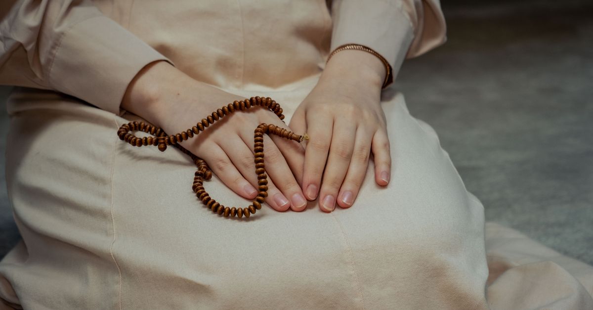 Gros plan sur les mains d'une femme tenant des perles de prière, symbolisant la dévotion.