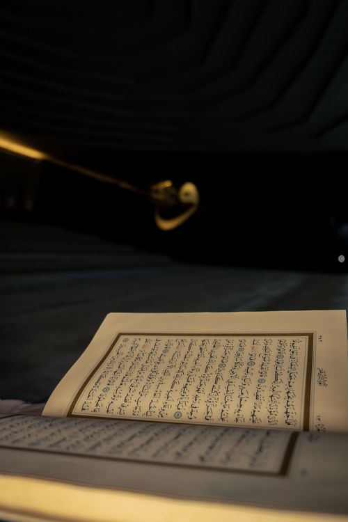 Free Close-up of an open Quran showing Arabic text inside a dimly lit mosque. Stock Photo
