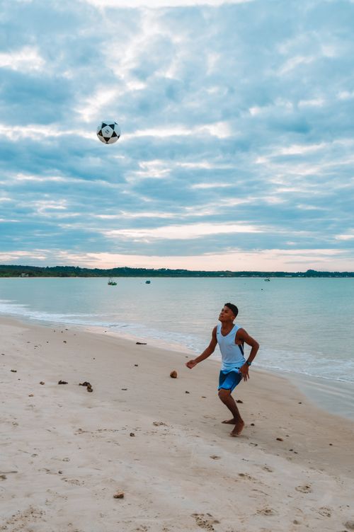 Free A young man enjoys playing soccer on a serene Brazilian beach under a cloudy sky. Stock Photo