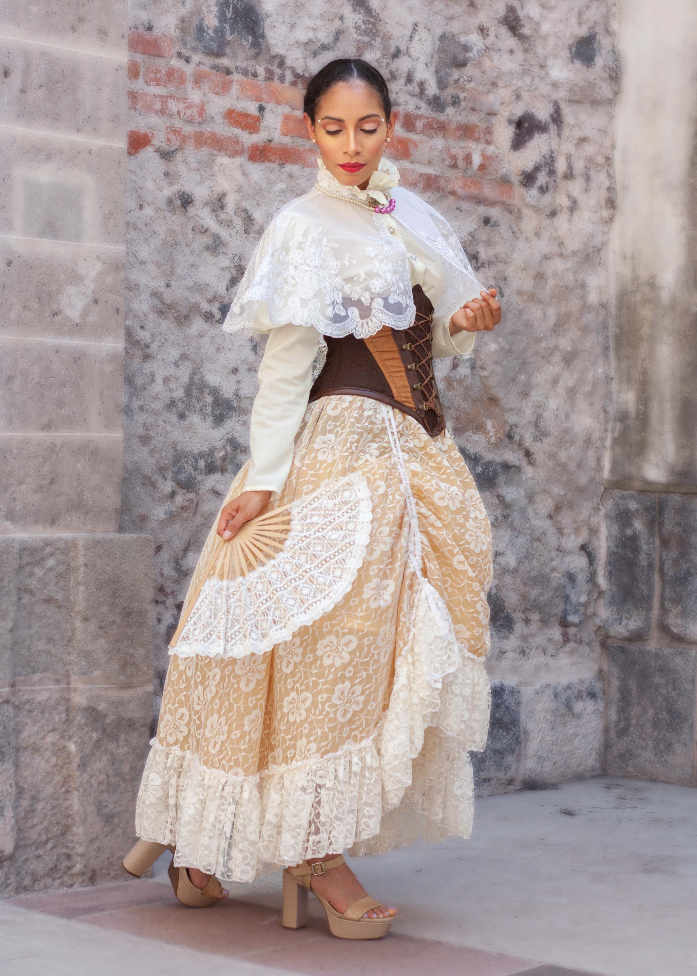 A woman in traditional lace attire poses against a rustic backdrop, holding a fan.