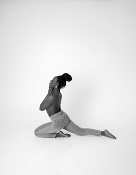 Black and white studio shot of a woman in a flexible pose wearing jeans, expressing art through form.