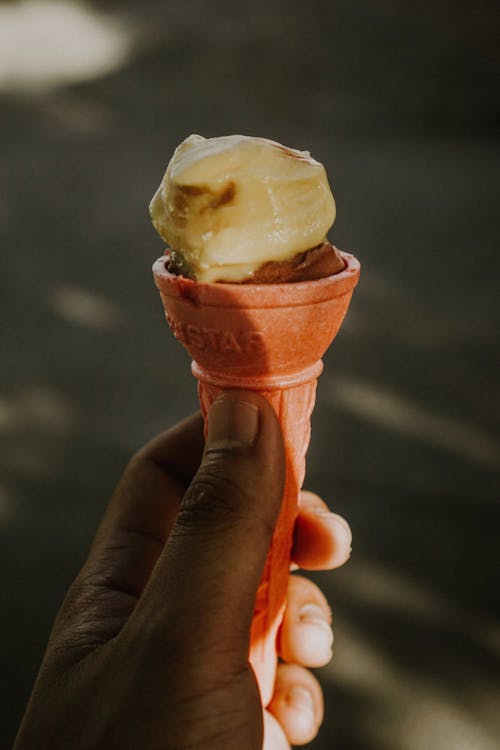 A hand holding an ice cream cone with a scoop of ice cream