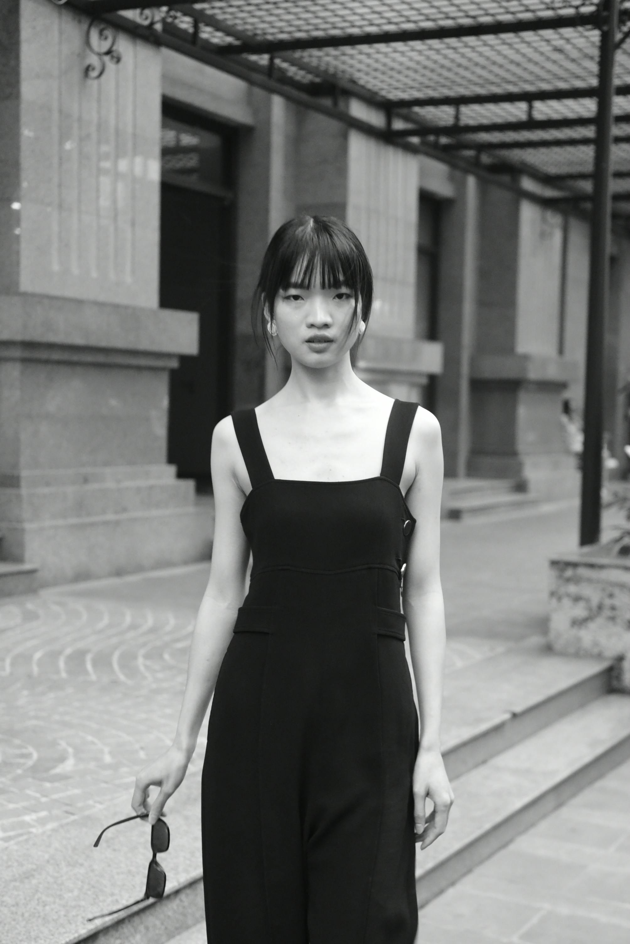 Fashionable urban portrait of an Asian woman in a stylish dress, captured in grayscale.