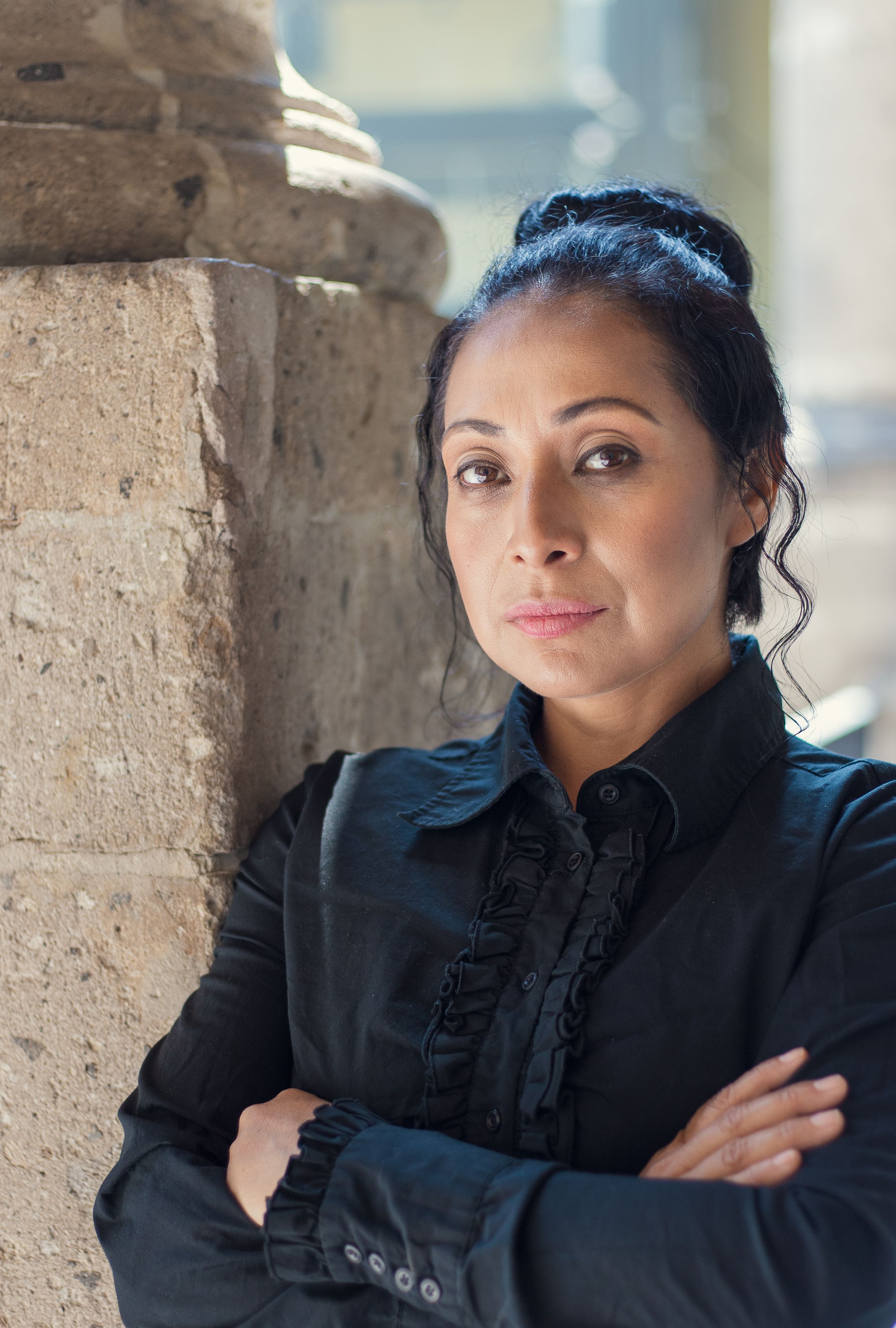 Elegant woman in a black shirt posing confidently against a stone wall in Ciudad de México.