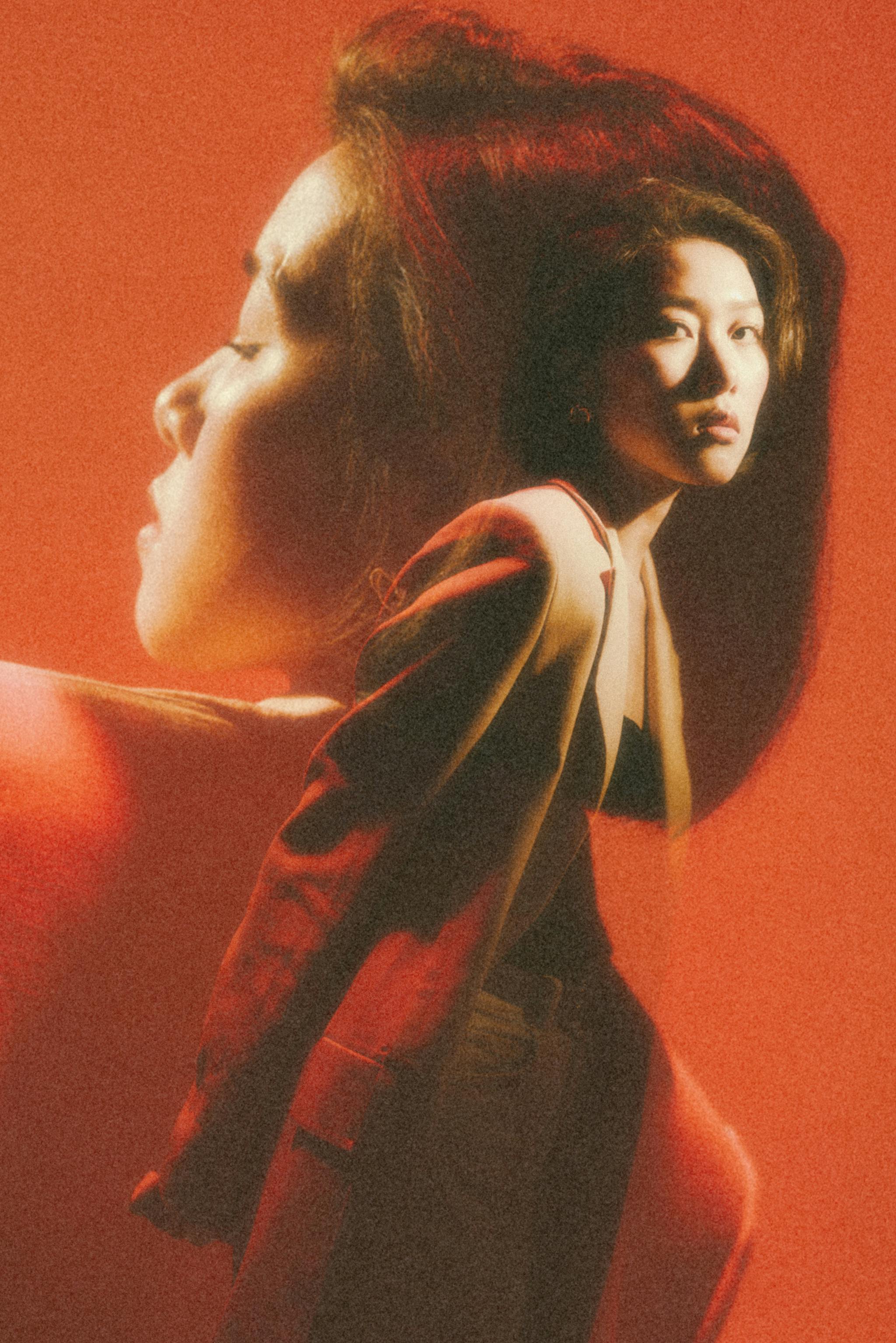 Artistic double exposure of an elegant woman in a beige jacket against a vivid red background.