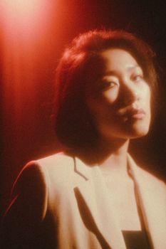 Artistic portrait of a woman in a beige jacket under red lighting, evoking a moody ambiance.