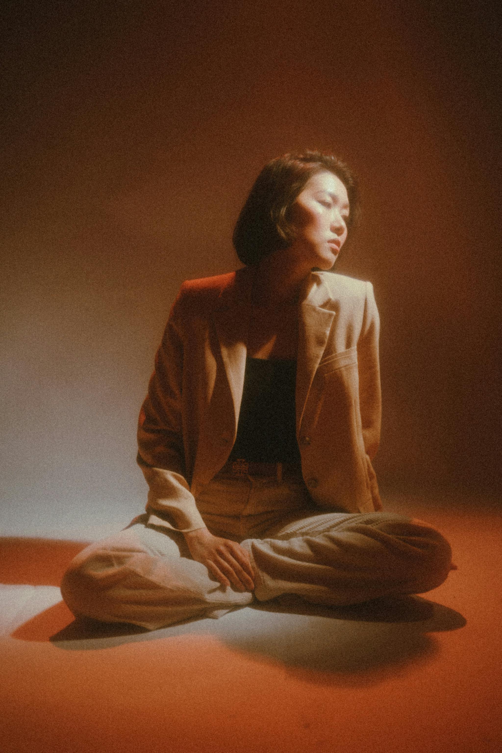 Asian woman in beige suit posing in studio with soft lighting, creating a moody and elegant atmosphere.