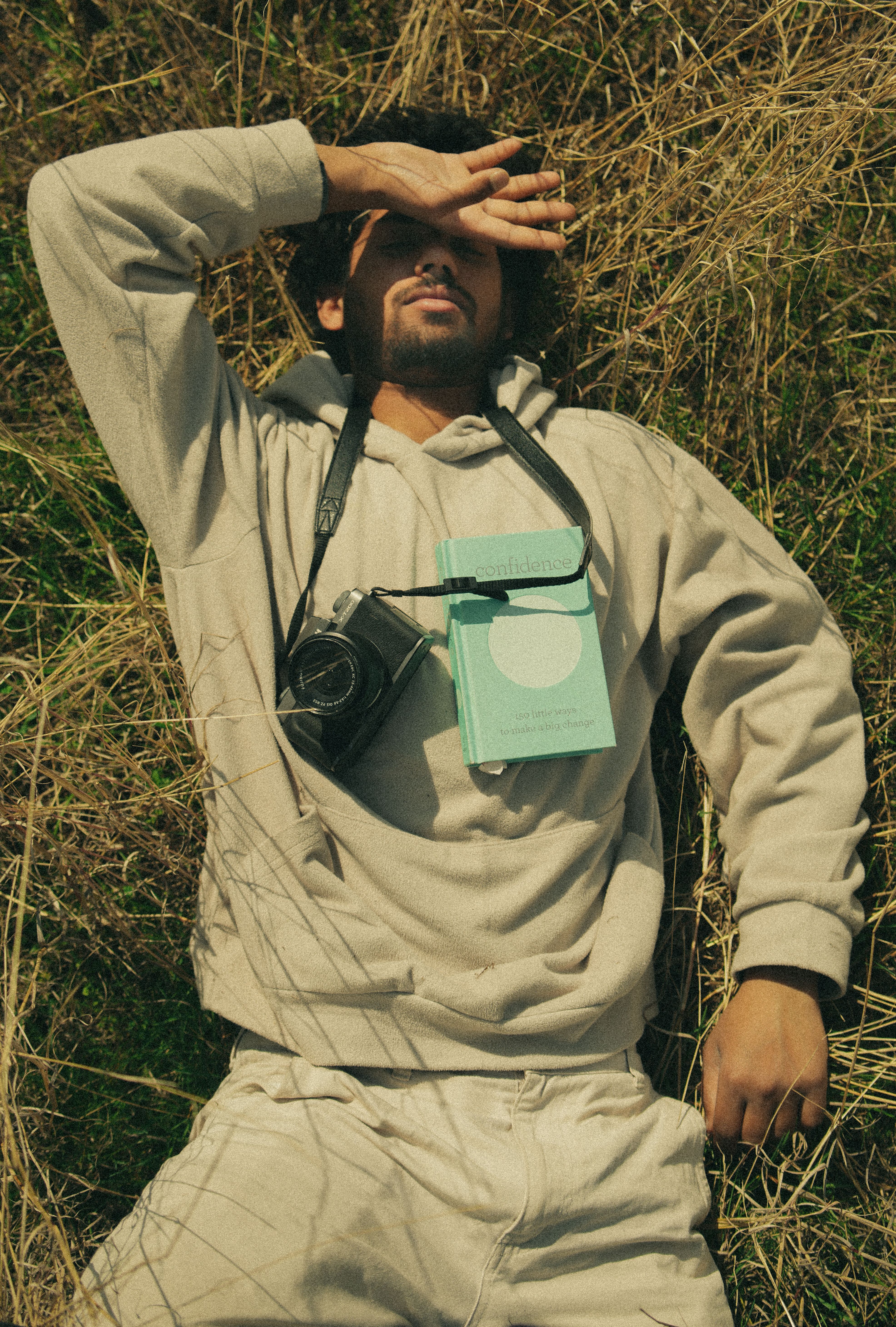 A man lying in a meadow with a camera and book, enjoying a peaceful moment.