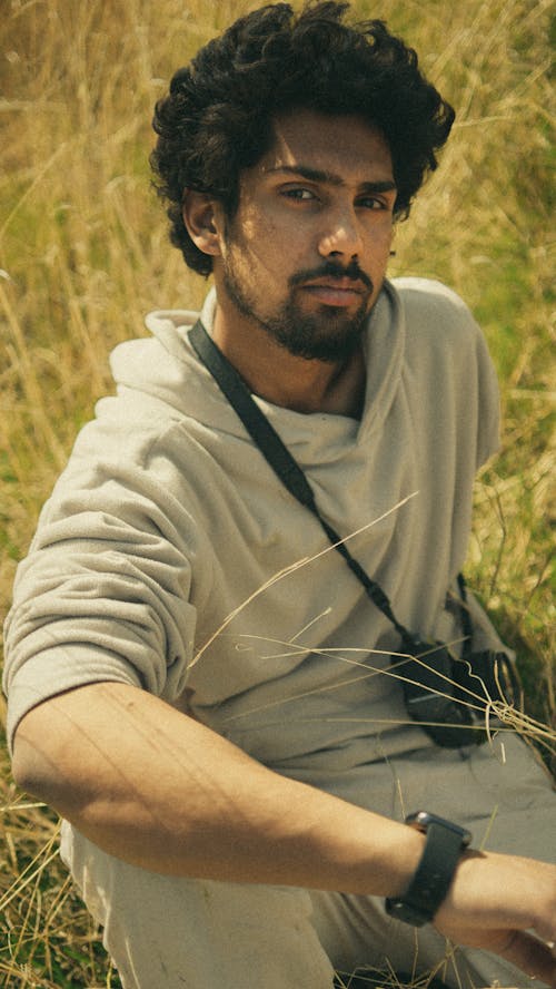 A man in a white shirt and grey sweater sitting in a field