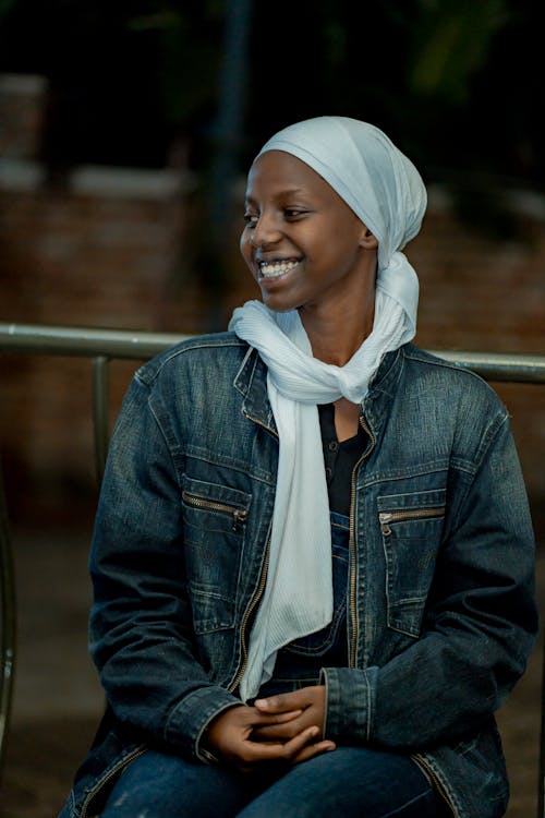 A smiling woman in a white headscarf and denim jacket