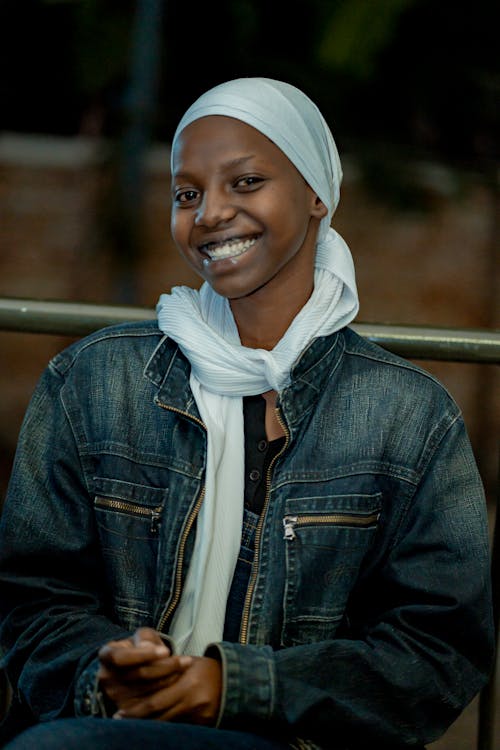 A smiling woman in a white headscarf and denim jacket