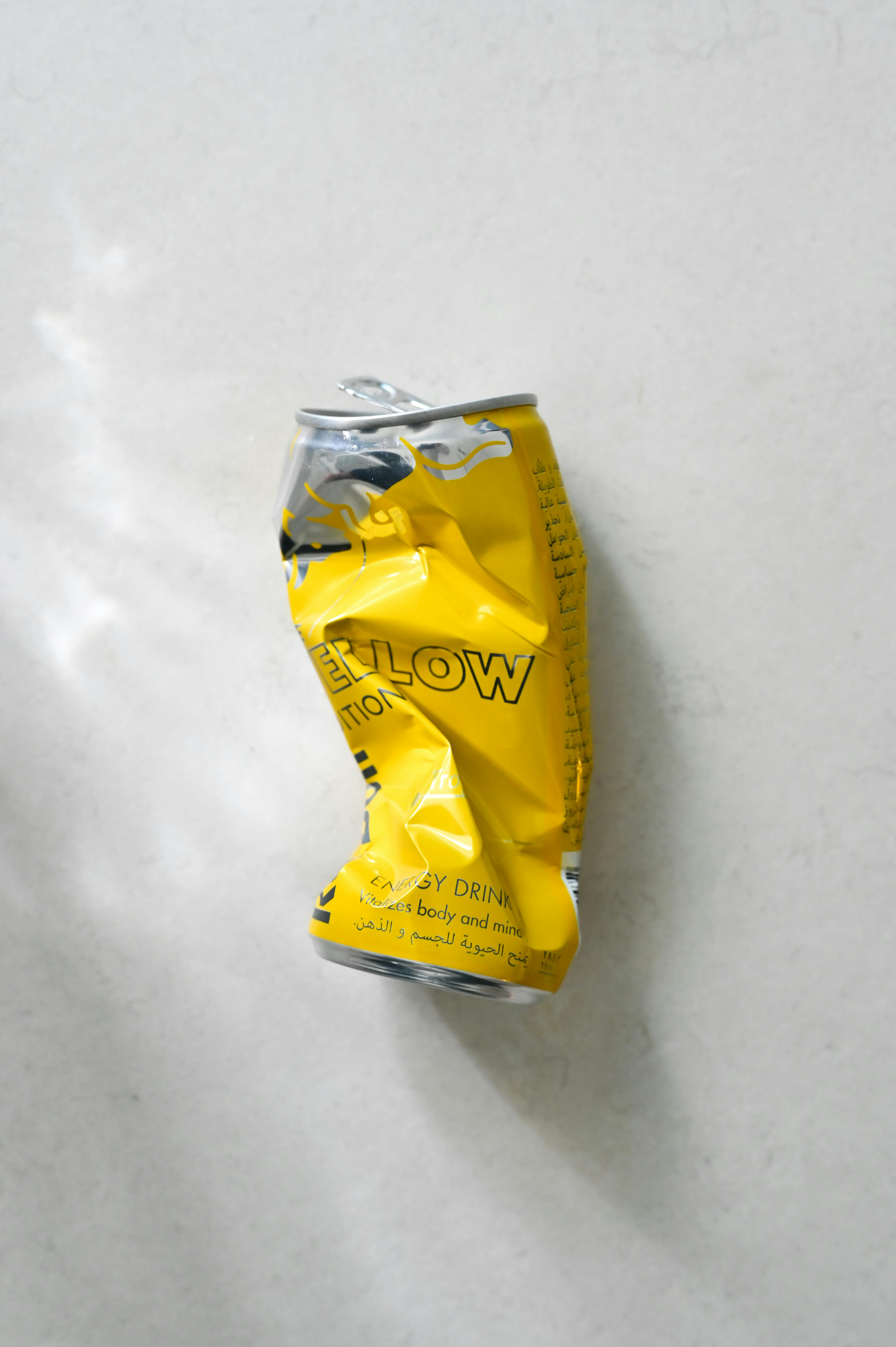 Crushed yellow energy drink can on a white surface, emphasizing recycling and waste.