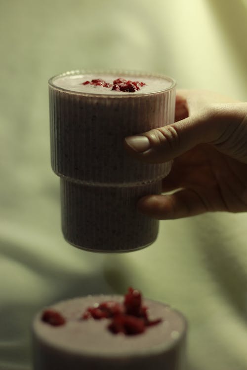 A person holding a glass of smoothie with raspberry