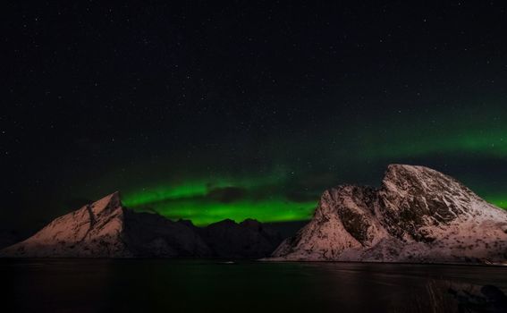 Breathtaking view of northern lights illuminating snowy mountains under a starry sky.