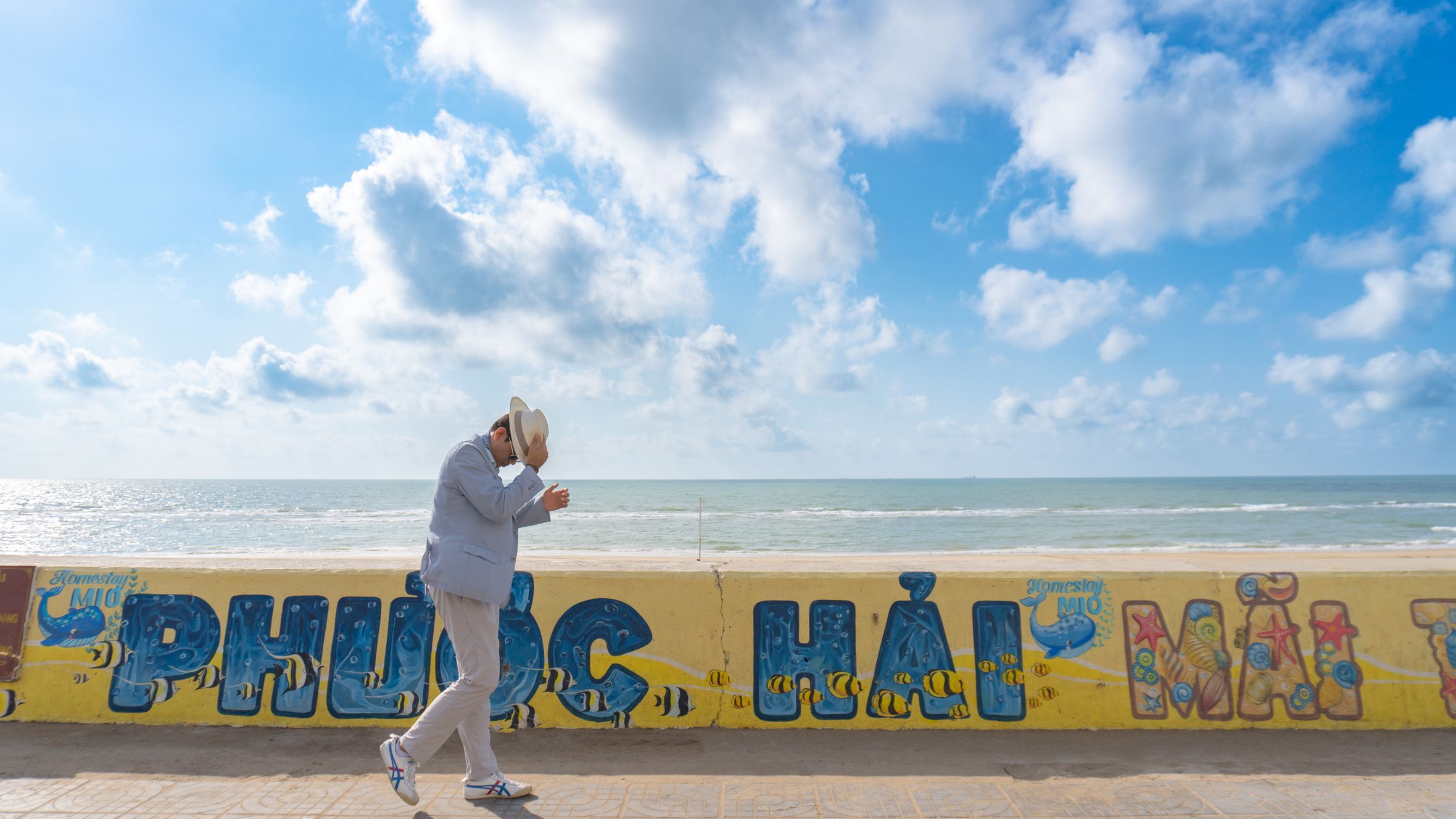 A man in a hat walks along a vibrant ocean promenade in Phước Hải, Vietnam.