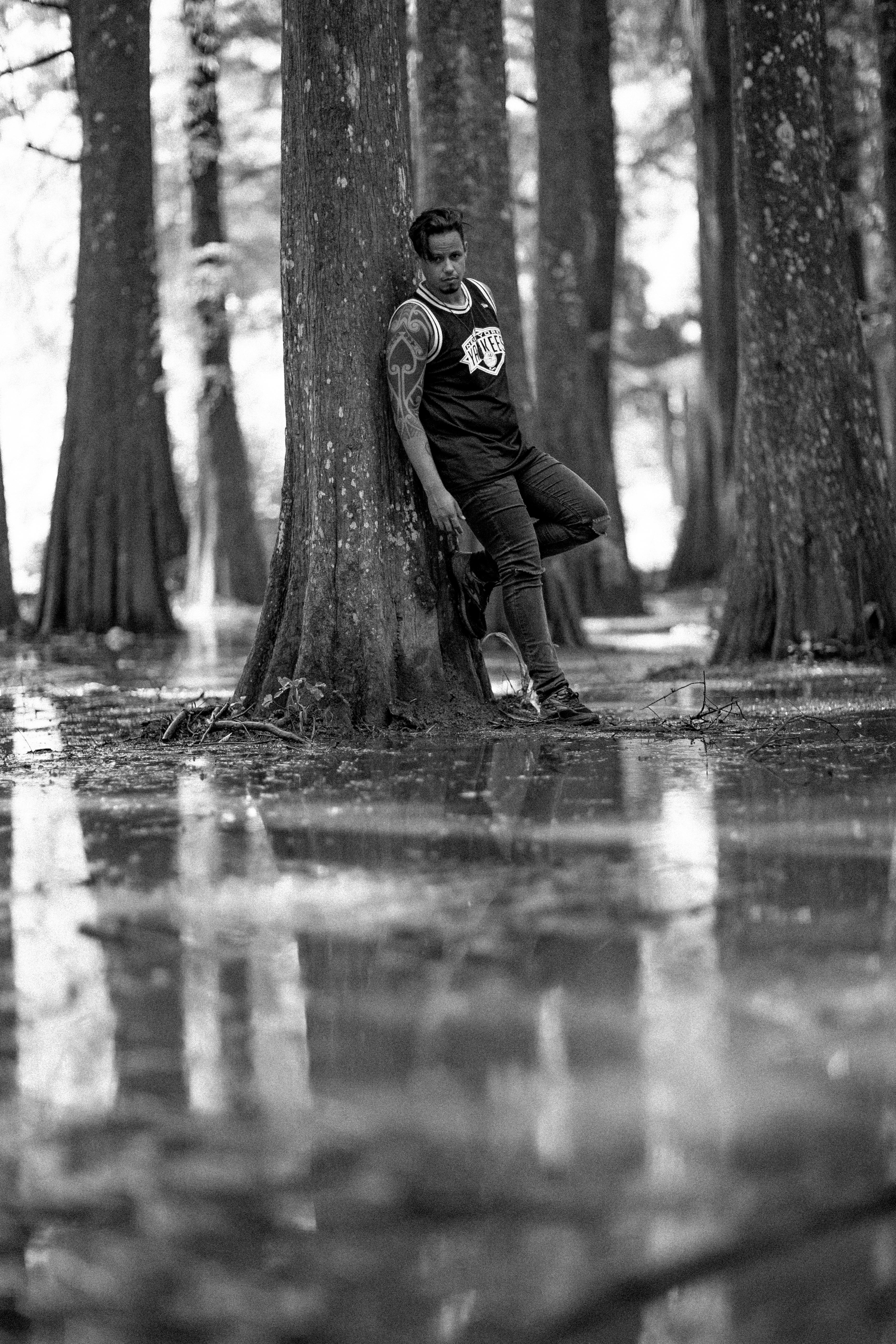 在反光的森林环境中，一名男子摆出姿势，形成一幅时尚的黑白肖像