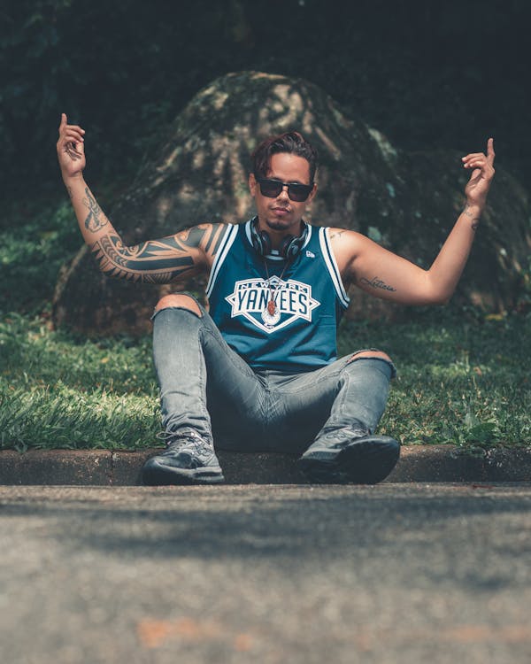 Man Sitting on Concrete Pavement Near Grassfield