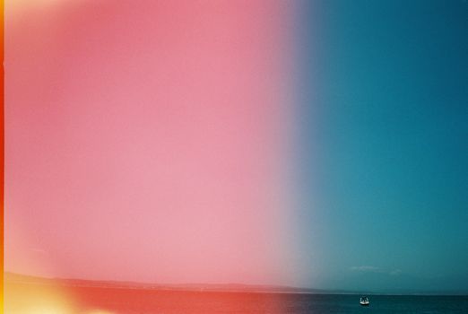 Vibrant abstract split of pink and blue hues over calm ocean waters.