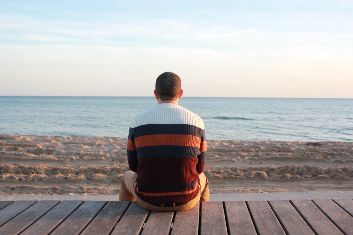 Free Man Sitting on Wooden Panel Facing in the Ocean Stock Photo