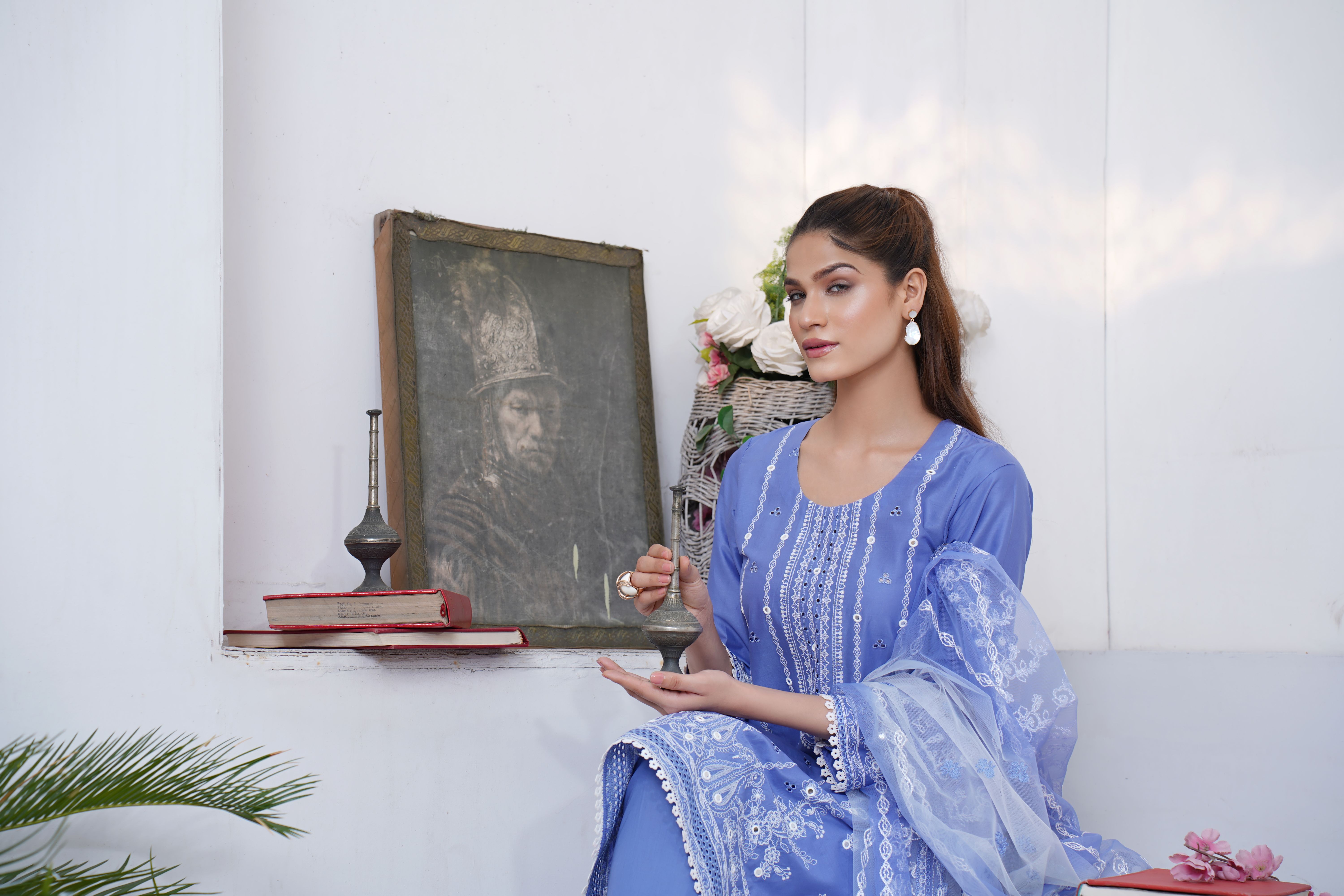 Portrait of a woman in Lahore wearing traditional clothing, holding an object, near a historical painting.