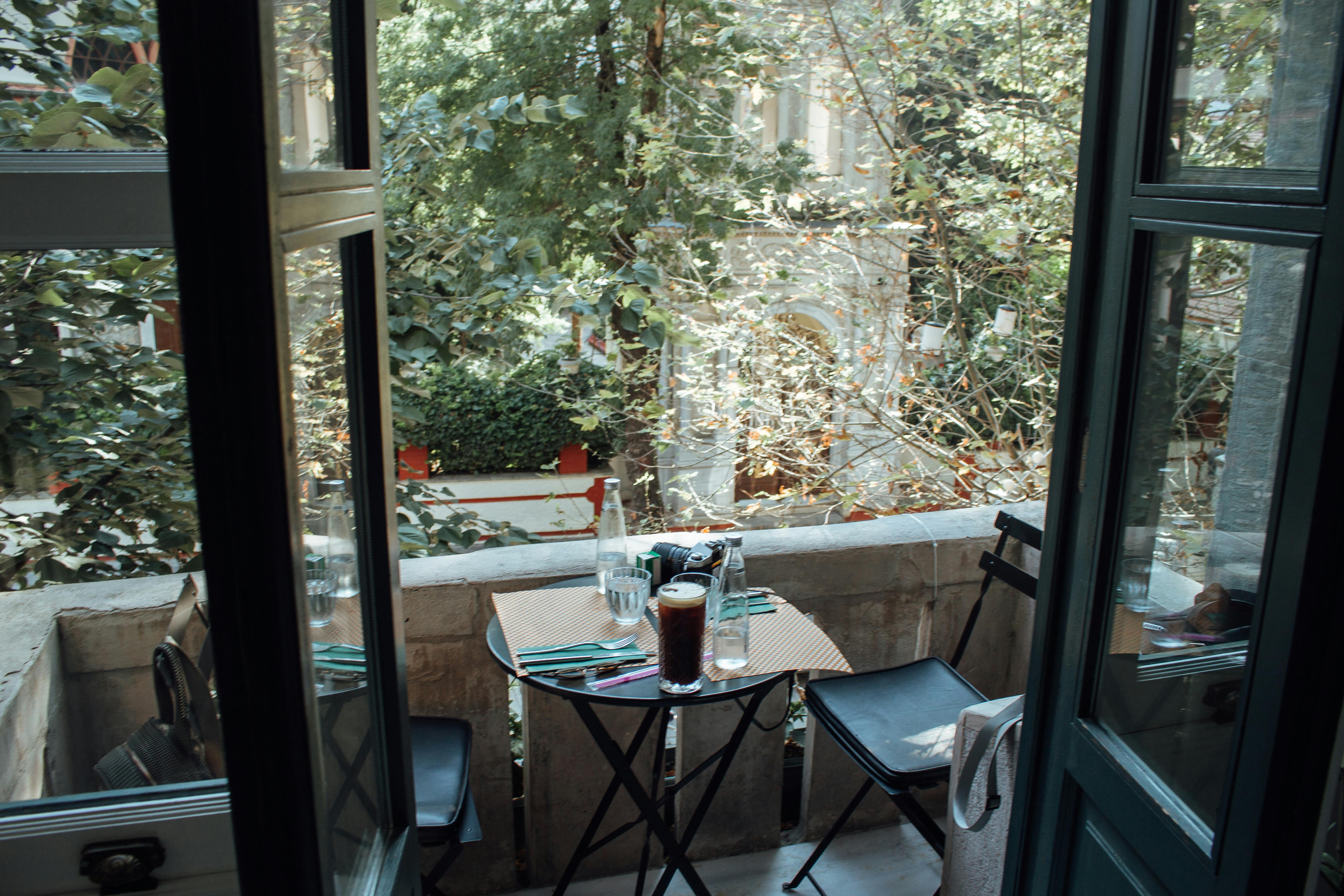 A folding wooden bistro set tucked into a sunlit balcony corner - compact balcony dining table