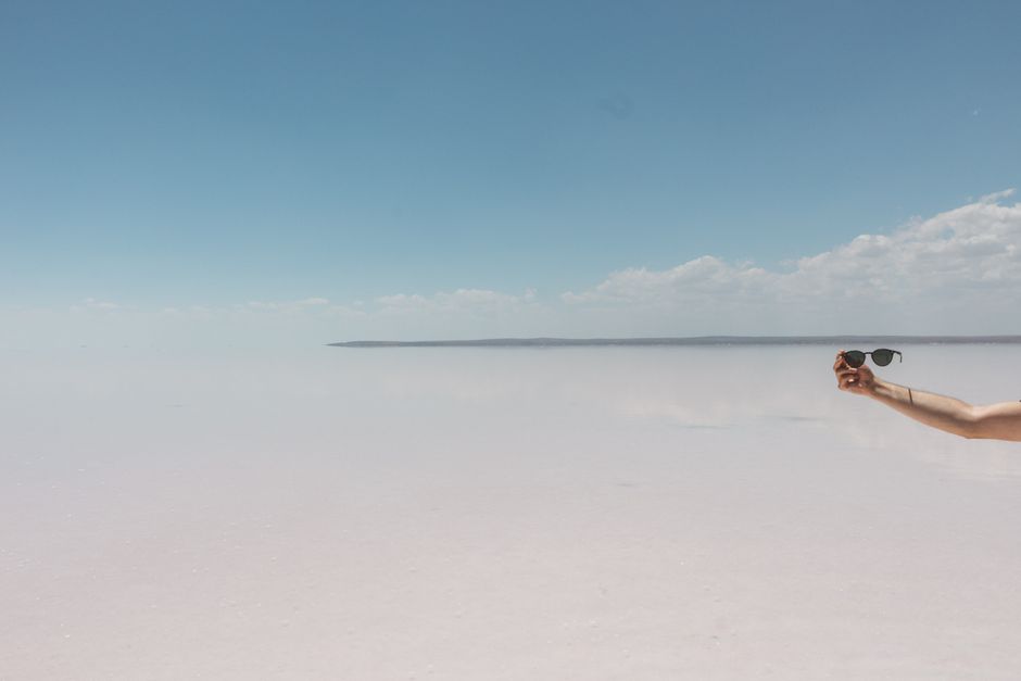 A serene beach landscape with a hand holding sunglasses against a clear sky.