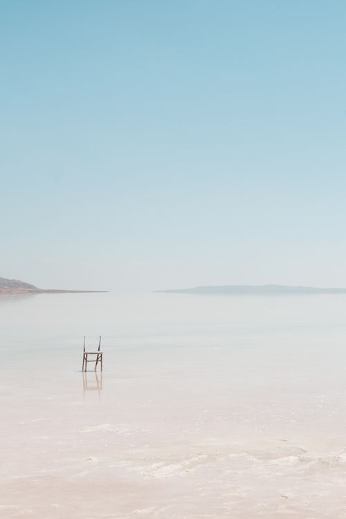 Free A solitary wooden chair stands on a misty beach, creating a serene and minimalist landscape view. Stock Photo