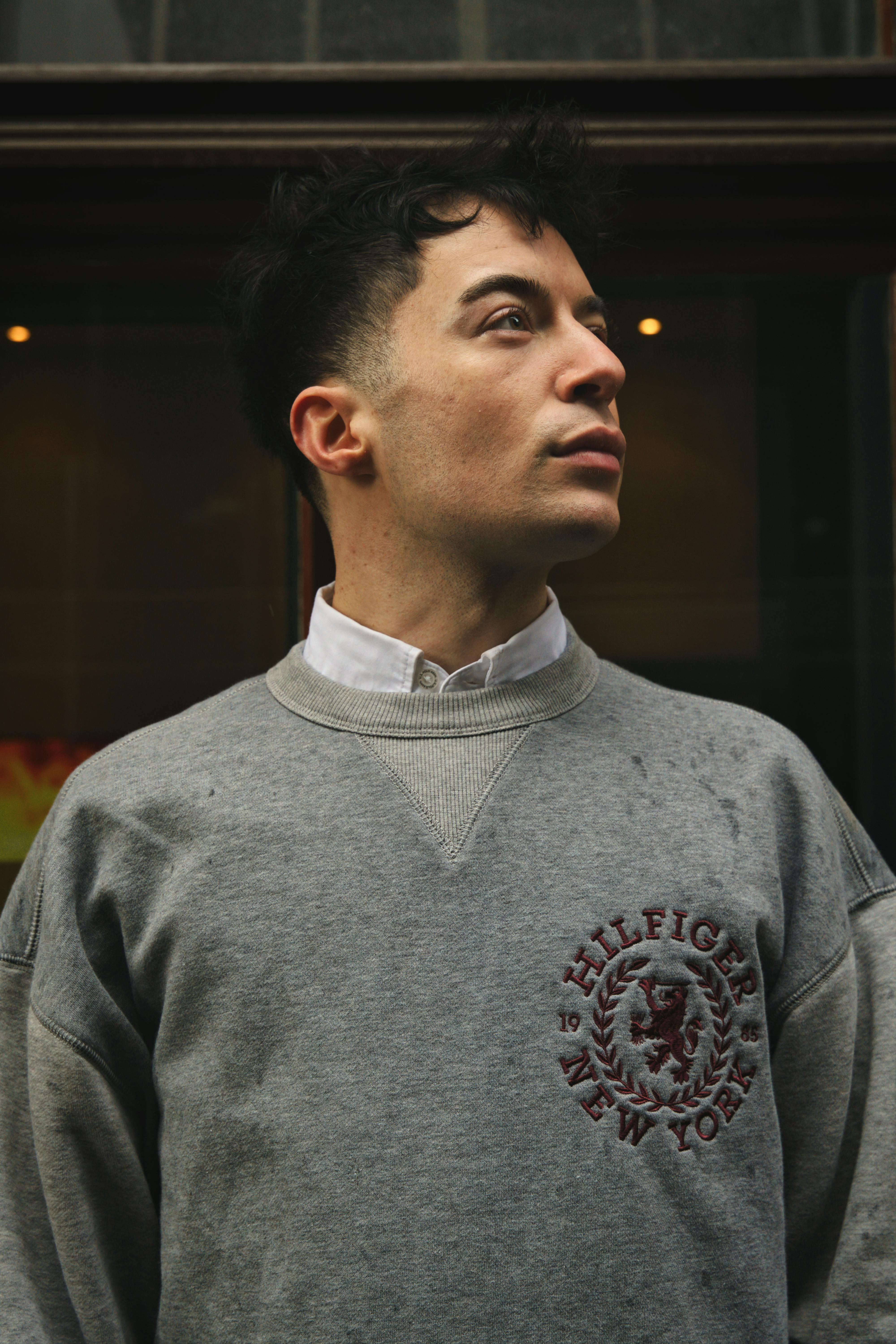 A man with dark hair poses confidently in a gray sweatshirt in Bremen, Germany.