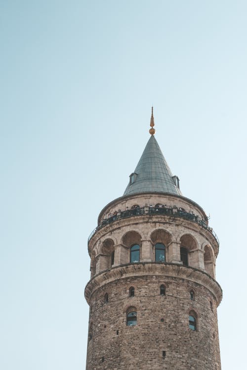 Low angle exterior of majestic old cone capped Galata Tower in Istanbul with arched windows against cloudless blue sky